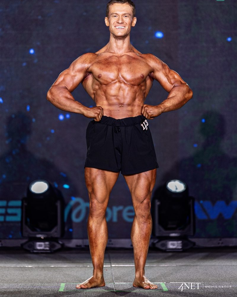 Cameron Kennison in a front pose as competitor 113 in Fit Physique.