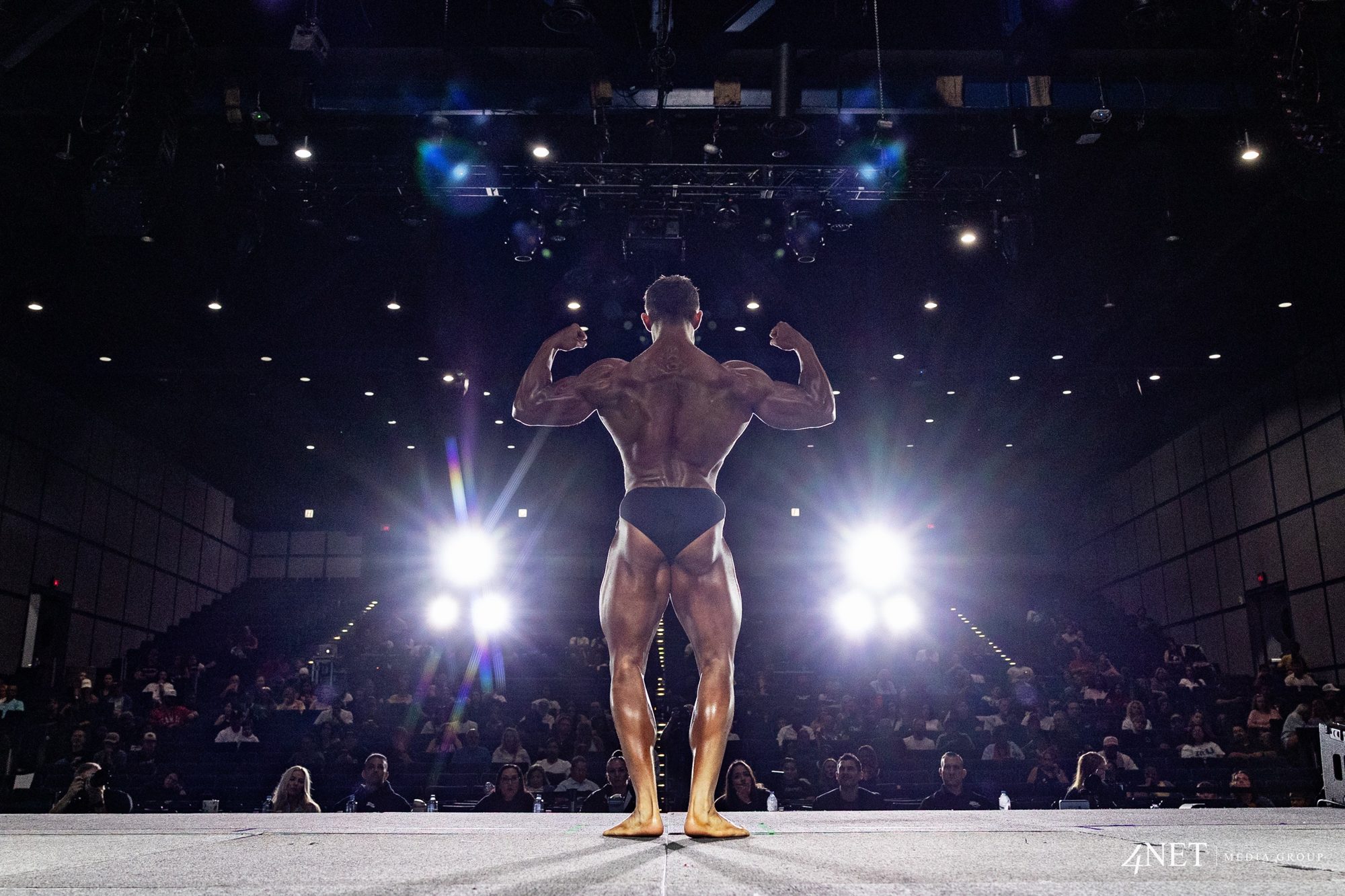 Cameron Kennison in a back double biceps pose, facing the lights and the crowd at Summer Shredding Houston.